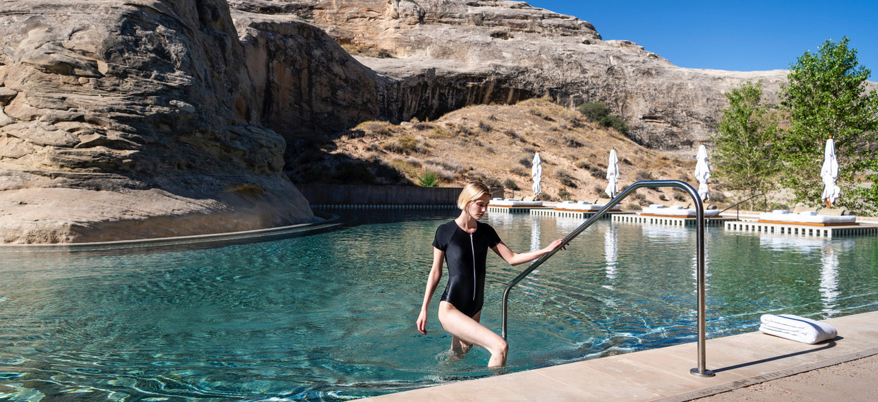 Model exiting a pool in the short sleeve coverswim one piece bathing suit.